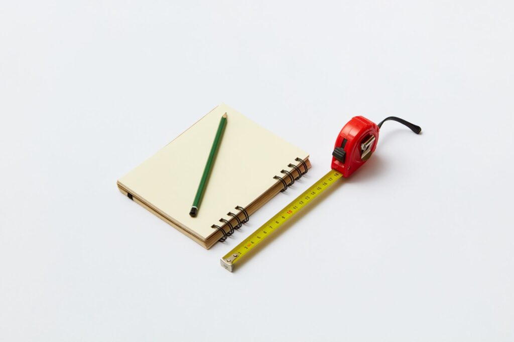 A notebook, tape measure, tray, and small plant pots arranged on a table for planning.