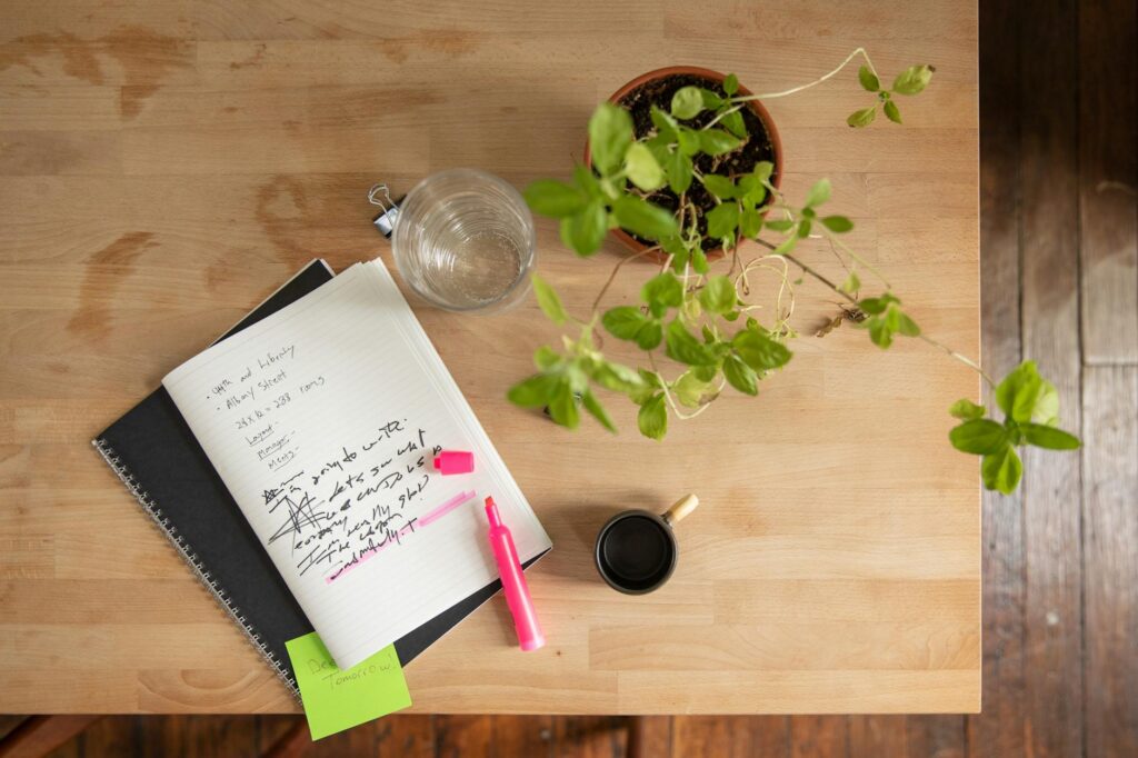 A notebook with watering notes beside a potted plant and a watering can